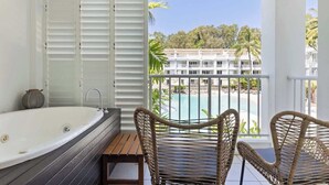 Un balcone con sedie in vimini, una vasca da bagno e vista su una piscina e degli edifici.