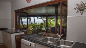 A kitchen with a view of the ocean, a sink, a stove, and a dish drying rack.