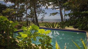 A swimming pool surrounded by lush greenery and a view of the beach.