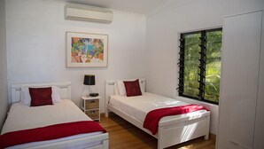 Una habitación con dos camas, una ventana con vistas a zonas verdes, un aire acondicionado instalado en la pared y un cuadro enmarcado.