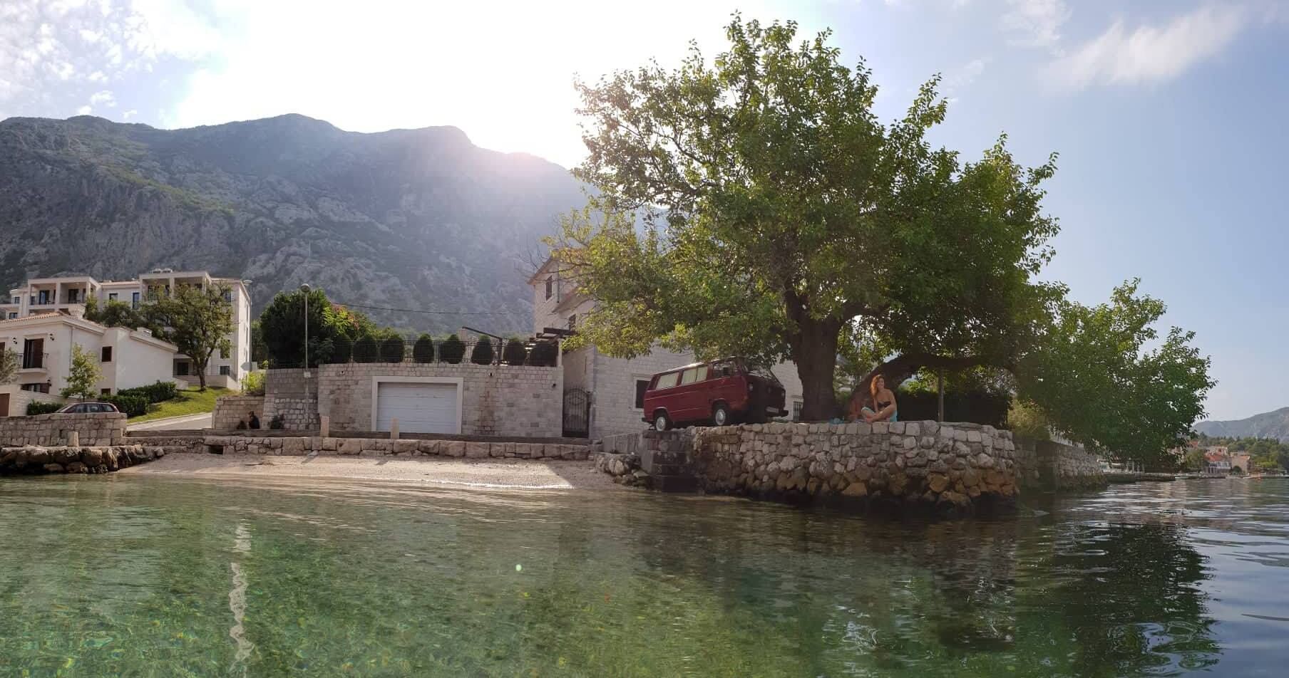Ein Objekt am Wasser mit einer Steinmauer, einem roten Lieferwagen und einem Baum.