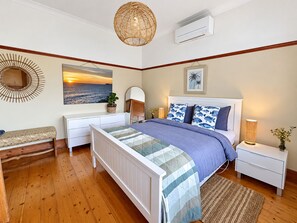 A bedroom with a bed, bedside tables, a bench, a wall-mounted air conditioner, and a hanging light fixture.