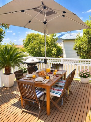An outdoor dining area with a table set for breakfast, surrounded by chairs, and an umbrella providing shade.