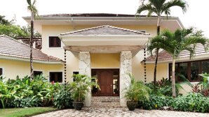 Un bâtiment à deux étages, doté d’une entrée pavée de pierres, d’un porche couvert et d’un aménagement paysager de style tropical.