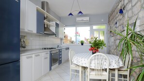 Une cuisine moderne avec des meubles blancs, une table à manger recouverte d’une nappe blanche et un mur en pierre.