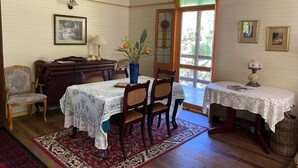 A dining room with two tables, chairs, a wooden desk, a lamp, and a vase with flowers.
