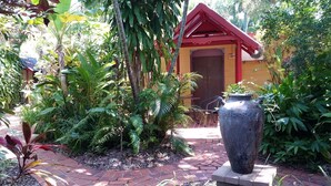 A garden with a red-roofed structure, a large decorative pot, and various tropical plants.