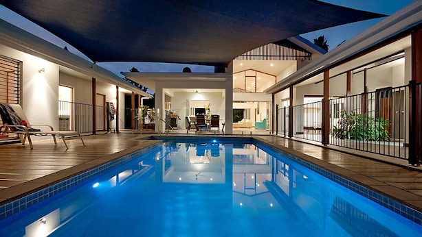 A swimming pool with a sunken seating area, a covered patio, and a view of the interior of the building.