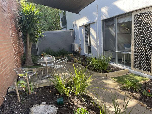 Un espace patio aménagé avec une table et des chaises, entouré de plantes et bordé d’un mur en briques.