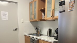 Ett kompakt kök med träskåp, ett kylskåp i rostfritt stål, en diskmaskin och en diskho med blandare.