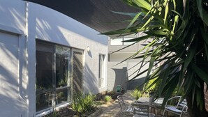 Ett modernt hus med en uteplats, inklusive en metallstol och ett metallbord, omgivet av växter och en liten trädgård.