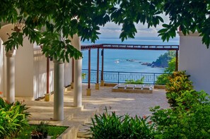 A covered outdoor area with a view of the sea, featuring a pergola structure and stone flooring.
