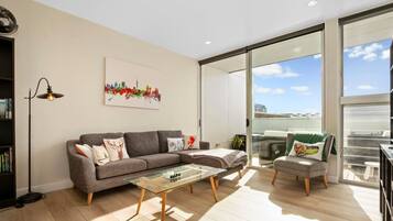A modern living room with a sofa, a glass coffee table, and a bookshelf.