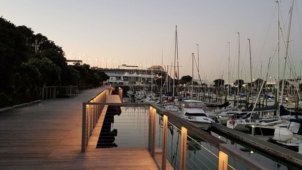 A marina with boats docked, a wooden walkway, and a building in the background.