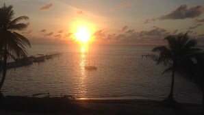 Ein Sonnenuntergang über einem ruhigen Meer mit Palmen und einer Anlegestelle.
