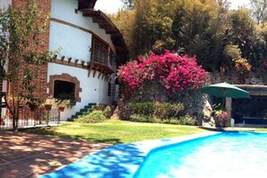 A pool area with a brick house, a well-maintained lawn, and a large bush of pink flowers. - Casa los Cuatro Manguitos for 10 guests 5 min away from lake & downtown (Valle de Bravo)
