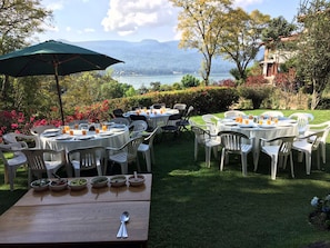 An outdoor dining area with round tables and chairs, set against a backdrop of a lake and mountains. - Casa los Cuatro Manguitos for 10 guests 5 min away from lake & downtown (Valle de Bravo)
