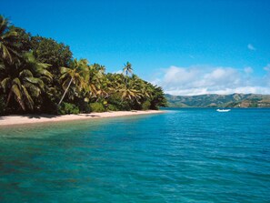 A beach with clear turquoise water, palm trees, and a boat in the distance. - Relax and unwind in paradise - absolute beach front holiday home (Nananu-i-ra)