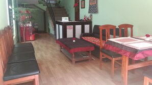 A reception desk with a 'RECEPTION' sign, a staircase, a dining area with wooden chairs and a table, and a green wall with framed artwork.