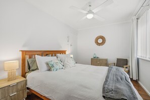 A neatly arranged bedroom with a bed, bedside table, lamp, and a small side table with a vase. - Salt & Sand - Flynn's Beach (Port Macquarie)