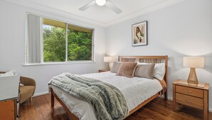 Une chambre à coucher avec un lit en bois, une table de chevet avec une lampe, une chaise et une fenêtre avec des rideaux.