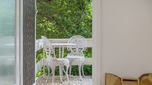 Un balcon avec des chaises et une table en métal peintes en blanc, un sol à motifs et une vue sur la verdure.