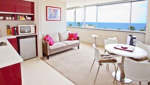 A modern apartment with a kitchen, a dining area, and a living room with a sofa and a view of the sea.
