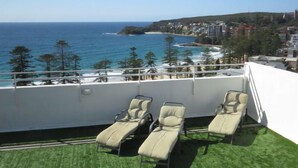 A balcony with three lounge chairs overlooking a coastal view.