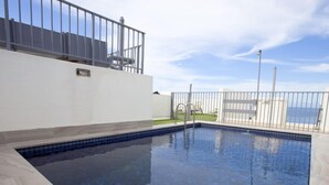 A swimming pool with a tiled edge, a metal fence, and a view of the sea.