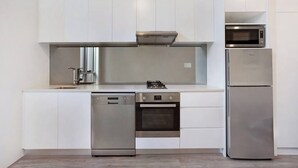 A modern kitchen with white cabinetry, a dishwasher, an oven, a microwave, and a refrigerator. - BONDI BEACH STUDIOS: VII (Bondi)