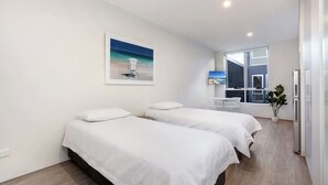 A modern hotel room with two beds, a large window with a view, a small seating area, and a potted plant. - BONDI BEACH STUDIOS: VII (Bondi)