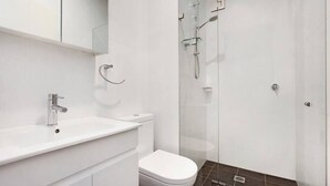 A modern bathroom with a white sink, toilet, and glass shower enclosure. - BONDI BEACH STUDIOS: VII (Bondi)