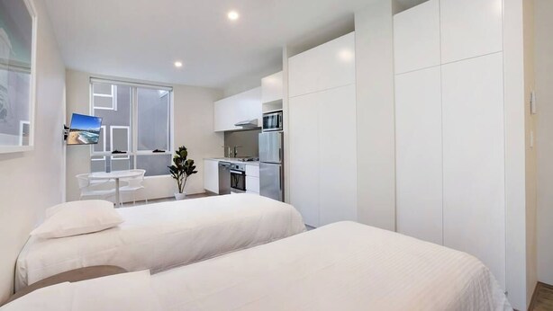 A modern hotel room with two beds, a small kitchenette, and a dining area with a table and chairs. - BONDI BEACH STUDIOS: VII (Bondi)
