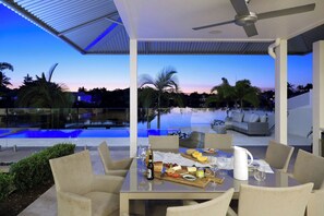 A dining area with a table set for a meal, overlooking a swimming pool and palm trees. - The Peninsula Secret (Noosaville)