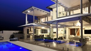Une maison moderne à deux étages dotée d’une piscine, d’un espace salon extérieur et d’un grand téléviseur dans le salon.