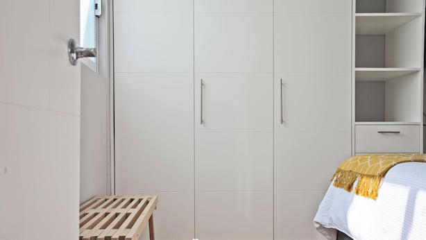 A bedroom with a bed, wooden bench, wardrobe, and a small table.