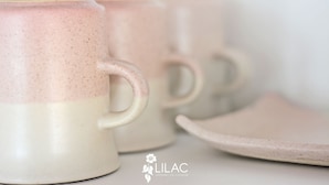 A close-up of ceramic mugs with a speckled design, a handle, and a logo with a flower and text.