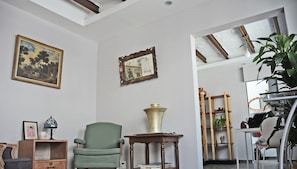 A room with a green armchair, a wooden side table with a brass vase, a framed mirror, and a painting on the wall. - Located In One Of The Oldest Streets Of The Historic Center Of Coyoacan (México D.F.)