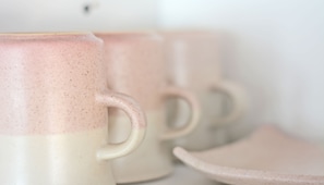 A close-up of ceramic mugs with a speckled design, a handle, and a logo with a flower and text. - Located In One Of The Oldest Streets Of The Historic Center Of Coyoacan (México D.F.)