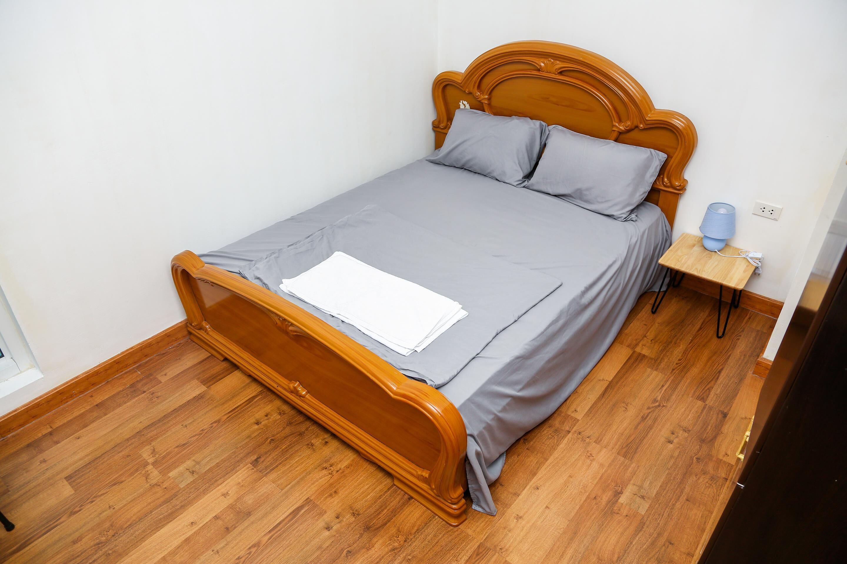 Een enkel bed met een houten hoofdbord en grijze beddengoed in een kamer met houten vloer.