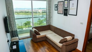 A living room with a large window, a brown sectional sofa, a flat-screen TV, and framed artwork on the wall.