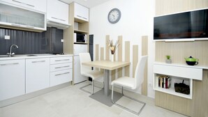 Une cuisine moderne avec des meubles blancs, une table à manger avec des chaises, une horloge au mur et un téléviseur à écran plat fixé au-dessus du comptoir.
