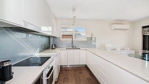 A modern kitchen with white cabinets, a built-in stove, and a window with blinds.