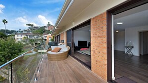 A modern balcony with a wicker chair, a glass railing, and a view of neighboring houses.