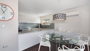 A modern kitchen with white cabinets, a glass dining table, and white chairs.
