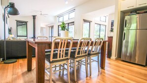Una cocina moderna con una mesa de comedor de madera, cuatro sillas, un ventanal grande y un refrigerador de acero inoxidable.