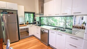 Una cocina moderna con armarios blancos, electrodomésticos de acero inoxidable y un amplio ventanal con vistas a la vegetación.