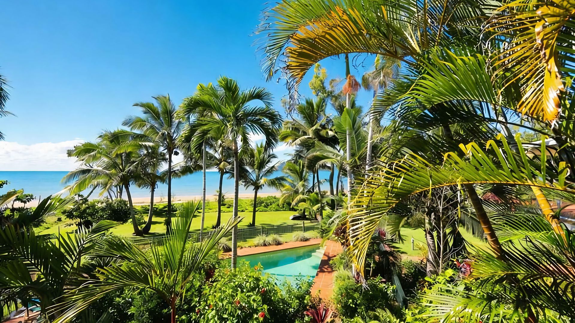A tropical resort with a pool, palm trees, and a view of the ocean.