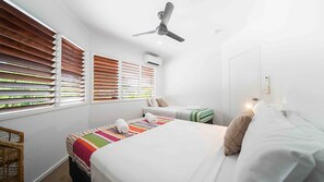 A bedroom with two beds, a ceiling fan, and a window with blinds.