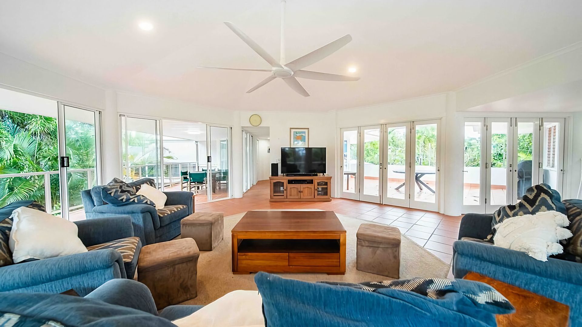 A spacious living room with a ceiling fan, a television on a wooden cabinet, and large sliding glass doors leading to an outdoor area.